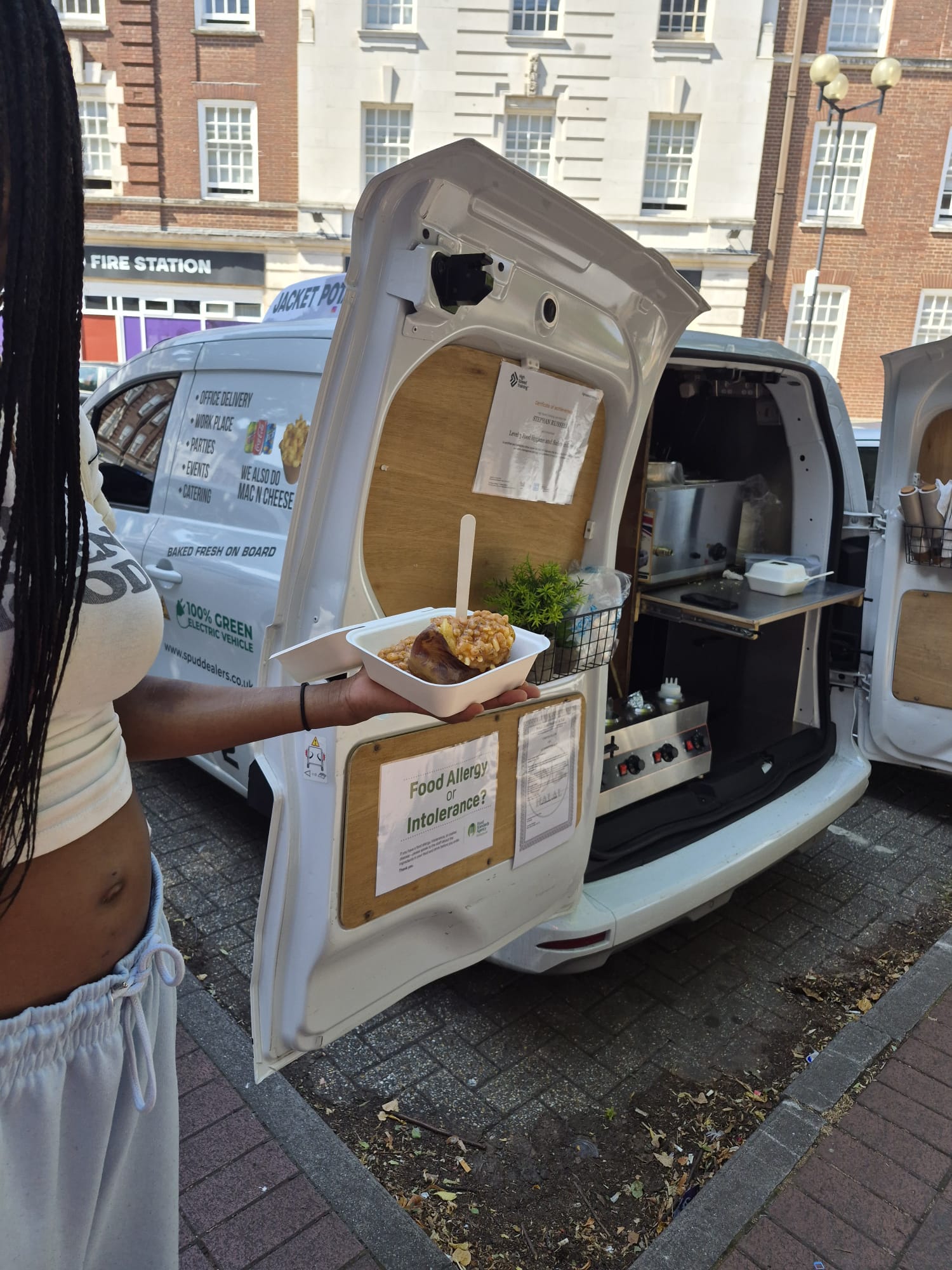 Customer holding a freshly baked jacket potato with cheese and beans at The Spud Dealers van